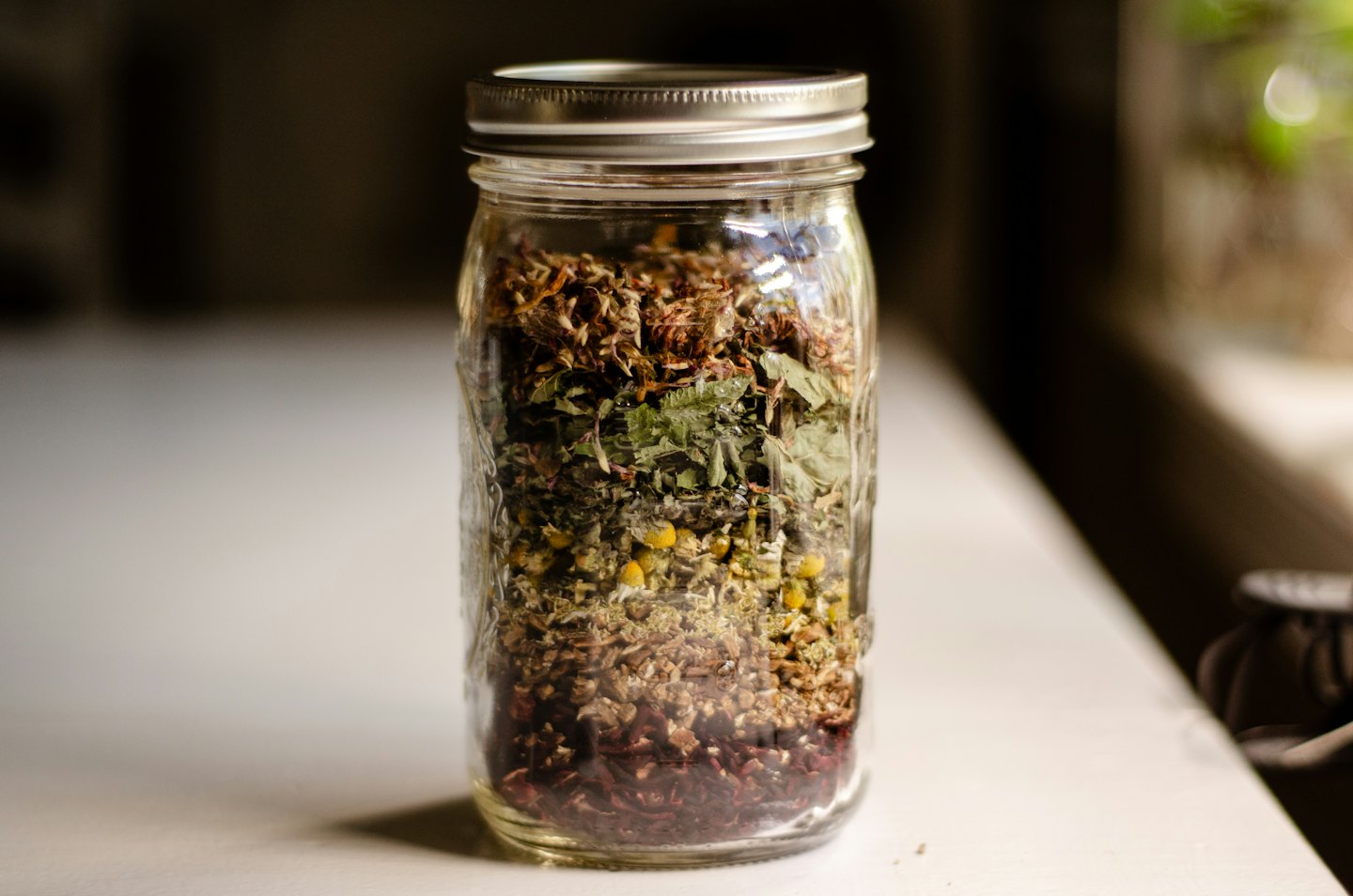 Bocal en verre rempli de couches d'herbes séchées et de fleurs.