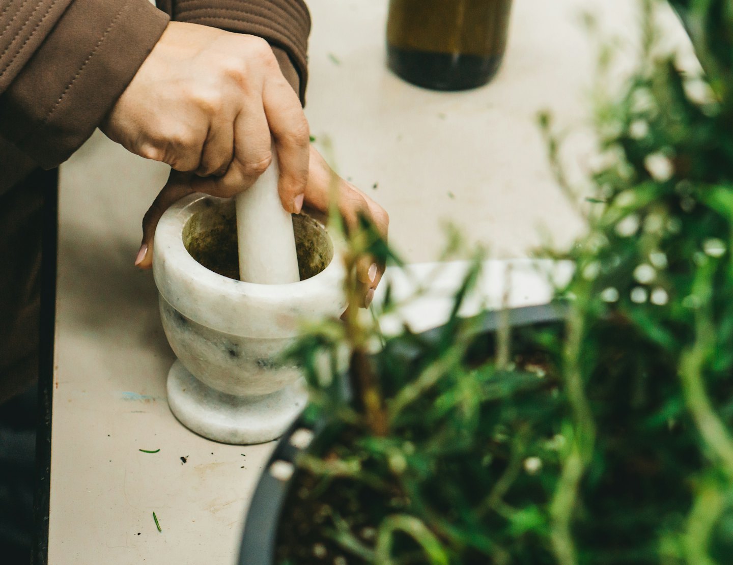 Des mains broient des herbes vertes dans un mortier en marbre blanc.